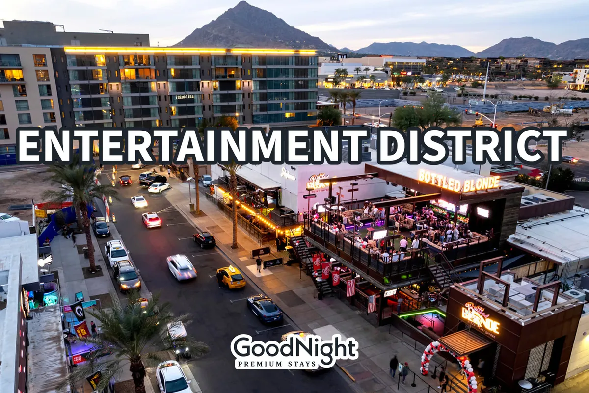 A vibrant street scene in the heart of the entertainment district, with prominent signage, bustling outdoor seating areas, and a lively crowd set against a mountain backdrop. The area exudes energy, suggesting active nightlife with dining, bars, and live entertainment options.