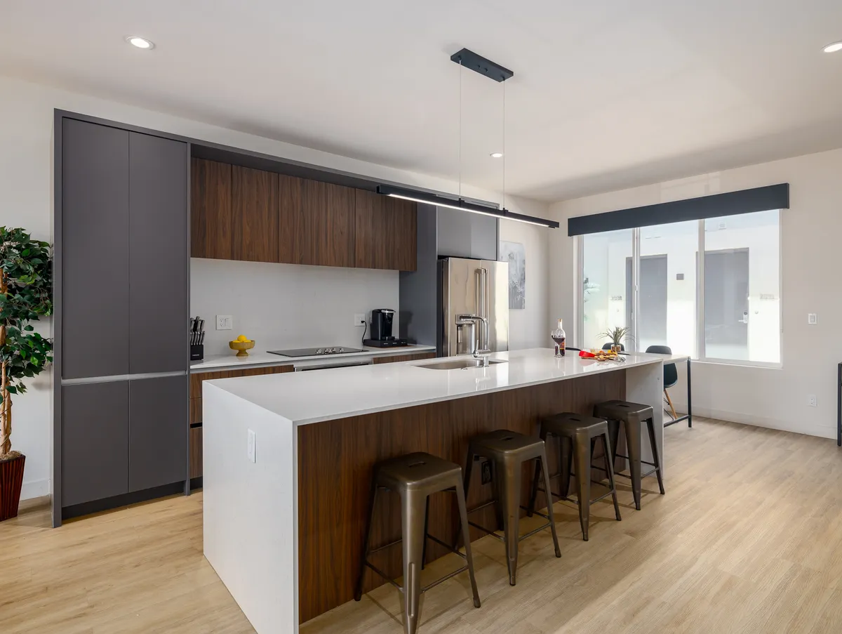 A spacious and contemporary kitchen with a large island featuring bar stools, surrounded by sleek cabinetry and modern appliances. The area is bathed in natural light from the large windows, creating an inviting environment for cooking and entertaining. The open concept allows for easy flow between the kitchen, dining, and living spaces.
