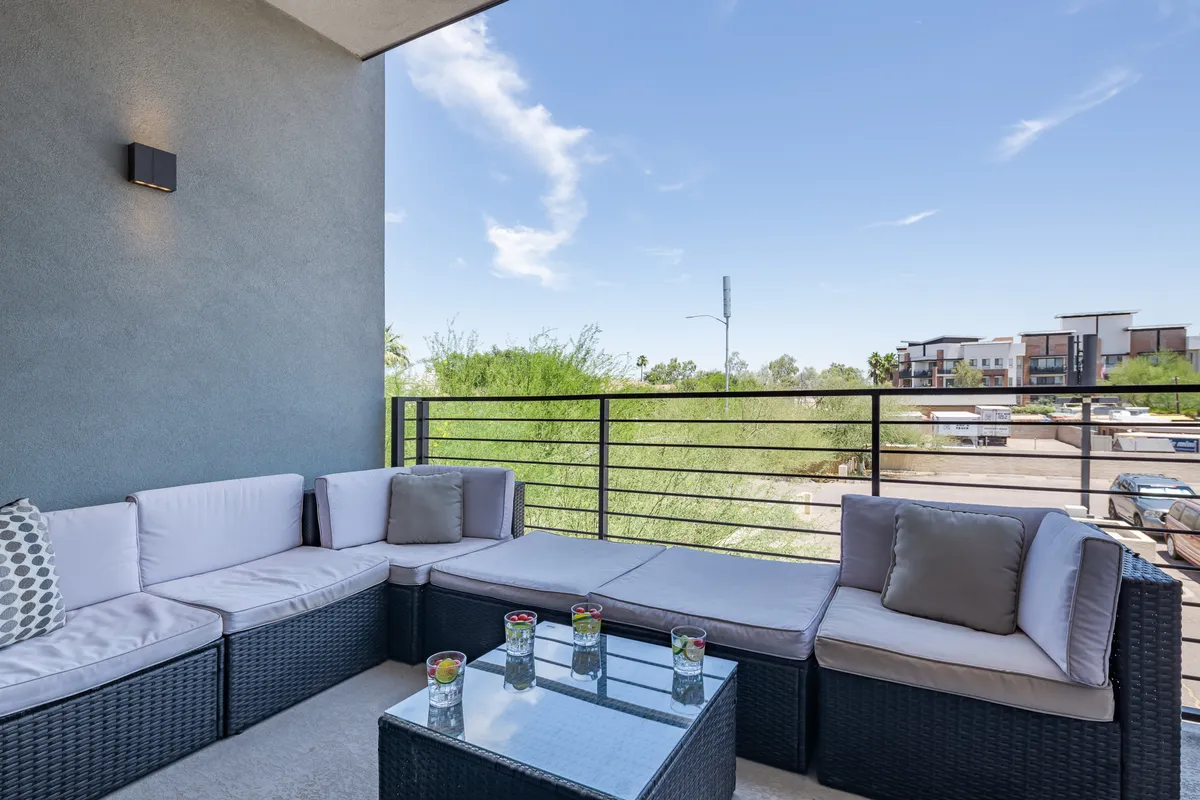 An inviting outdoor seating area featuring a glass coffee table and lush greenery, ideal for relaxing, socializing, or enjoying drinks. The scene is sunlit and offers an accessible, resort-style ambiance that evokes the comfort of home with the amenities of a stylish getaway.