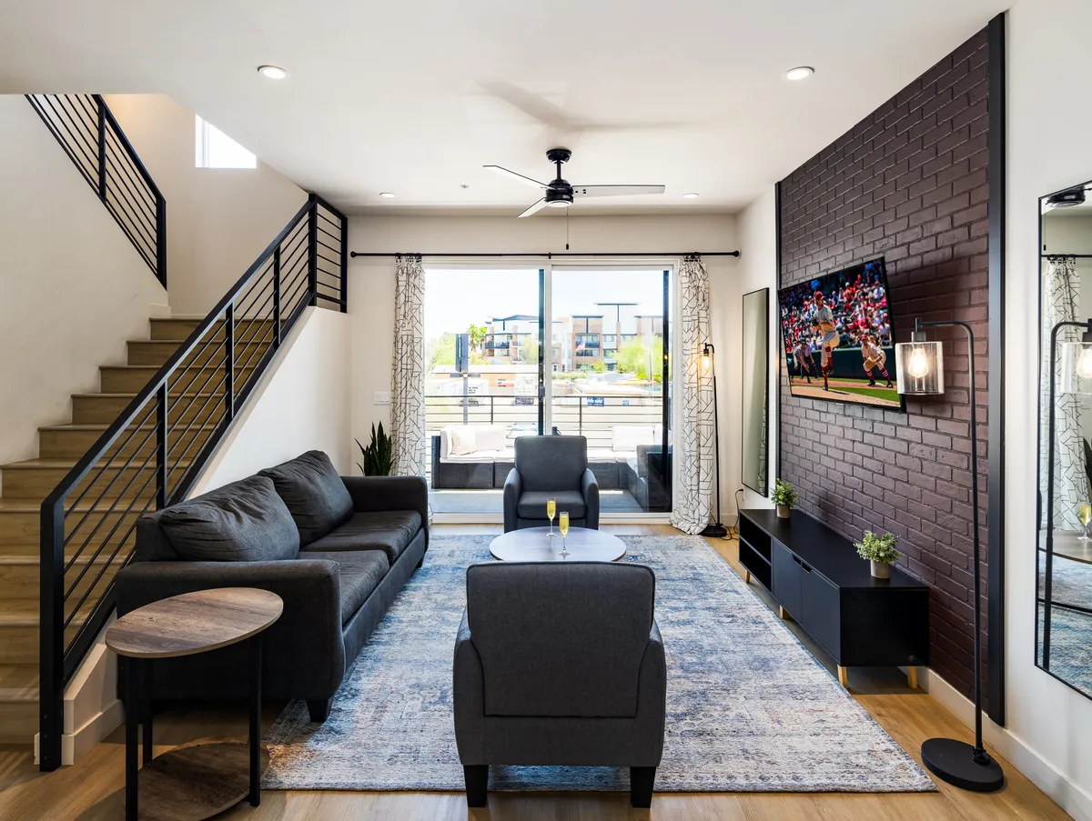 The image features a spacious, contemporary living room with a comfortable sofa, stylish coffee table, and a large television, all opening out to a private balcony with inviting sunset views. The setting is perfect for relaxing, socializing with friends, or enjoying entertainment, all in a bright and modern space.