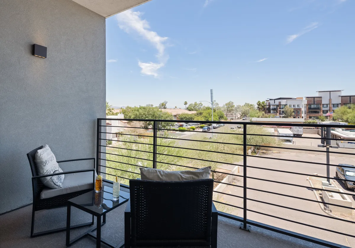 An inviting private balcony setup with comfortable chairs and a small table overlooking the surrounding area and open skies. The tranquil scene suggests a perfect setting for casual meetings, relaxing, or socializing after a busy day.