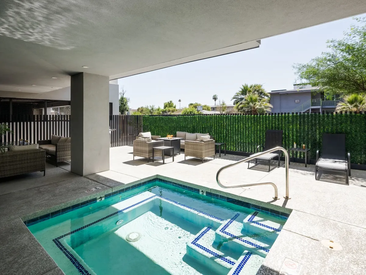 An exterior view of a tranquil outdoor area featuring a jacuzzi surrounded by comfortable seating and lush greenery. The scene is set for relaxation and entertaining, with the jacuzzi being the centerpiece for gatherings or quiet moments alike.