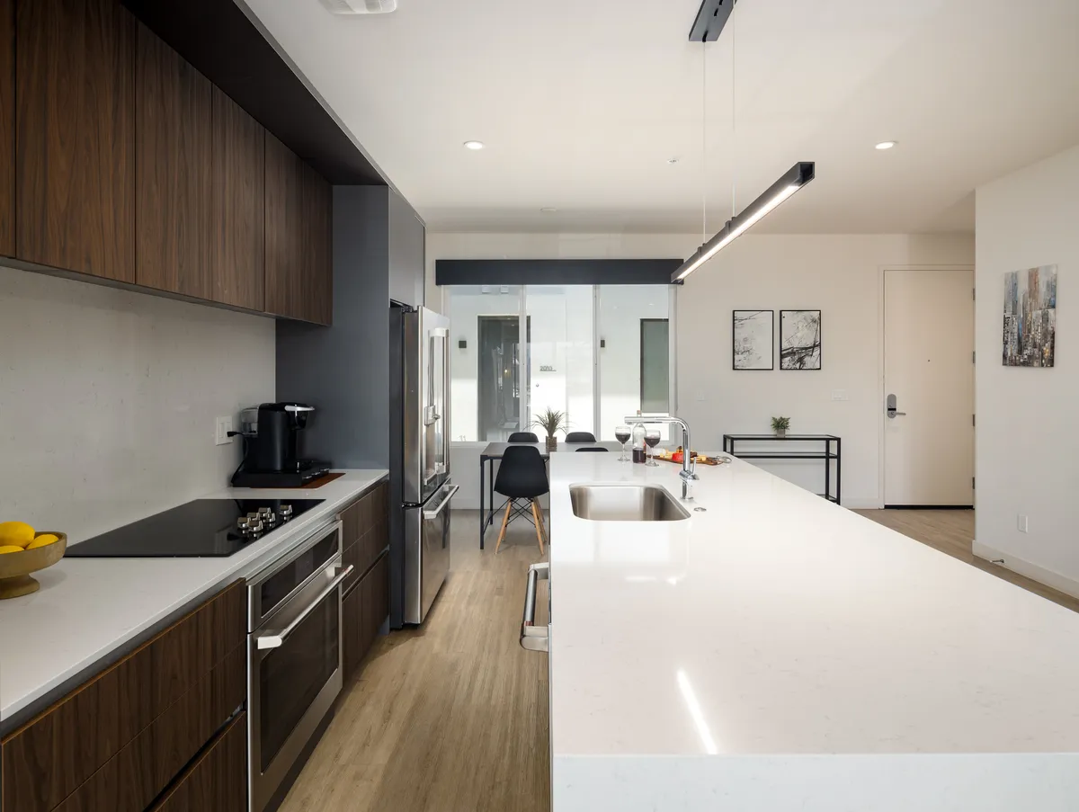 A modern kitchen featuring a spacious island, sleek appliances, and a bright, functional dining area. The surfaces are clear and ready for use, with subtle hints of convenience like accessible storage and modern lighting.